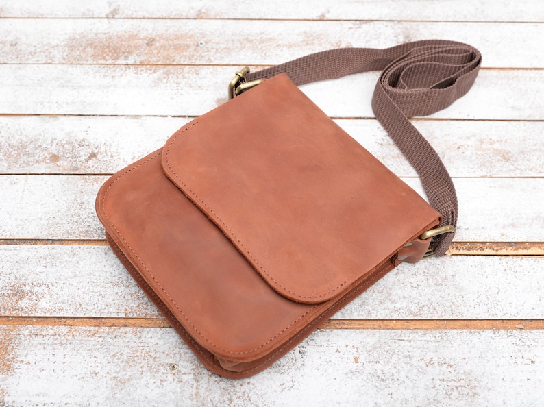May include: A brown leather crossbody bag with a flap closure and a brown adjustable strap.