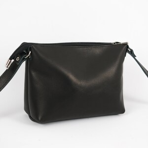 May include: A black leather crossbody bag with a zipper closure and a long adjustable strap.