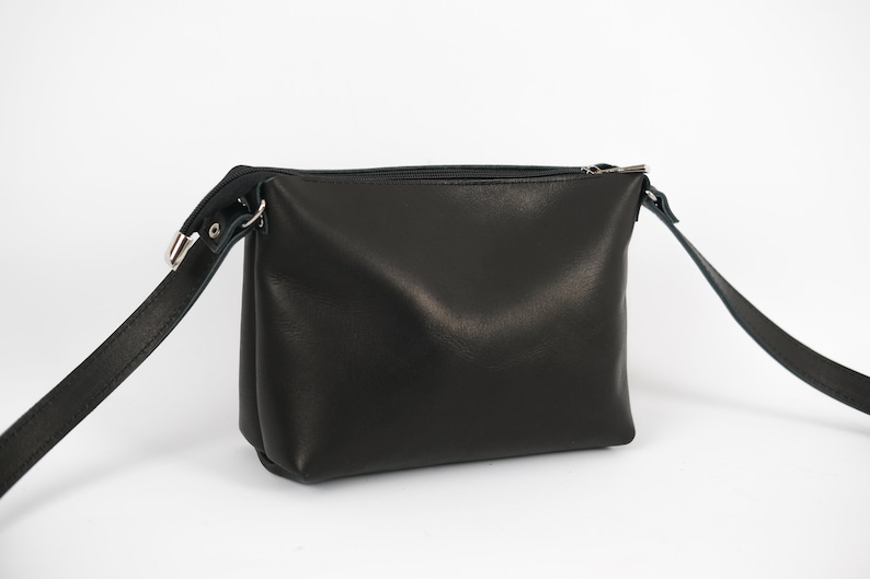 May include: A black leather crossbody bag with a zipper closure and a long adjustable strap.