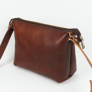 Pu&ograve; includere: Una borsa a tracolla in pelle marrone con chiusura a zip e una lunga tracolla regolabile.