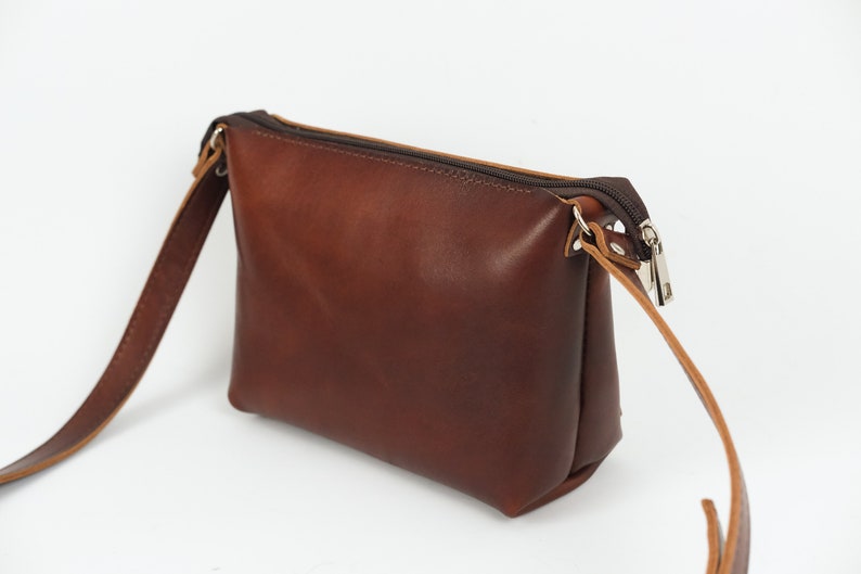 Pu&ograve; includere: Una borsa a tracolla in pelle marrone con chiusura a zip e una lunga tracolla regolabile.