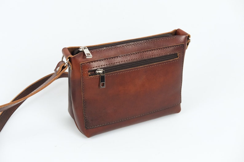 May include: A brown leather crossbody bag with a zippered pocket on the front. The bag has a long adjustable strap.