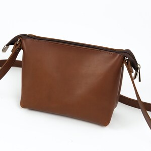May include: A brown leather crossbody bag with a zipper closure and a long adjustable strap.