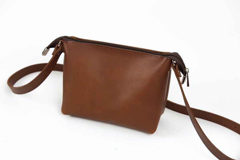 May include: A brown leather crossbody bag with a zipper closure and a long adjustable strap.