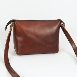 May include: A brown leather crossbody bag with a zipper closure and an adjustable strap.