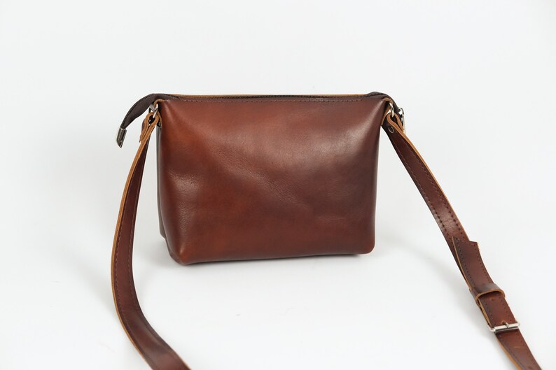 May include: A brown leather crossbody bag with a zipper closure and an adjustable strap.