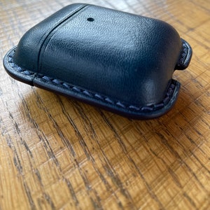Puede incluir: Una funda de cuero azul oscuro con un borde cosido para AirPods.