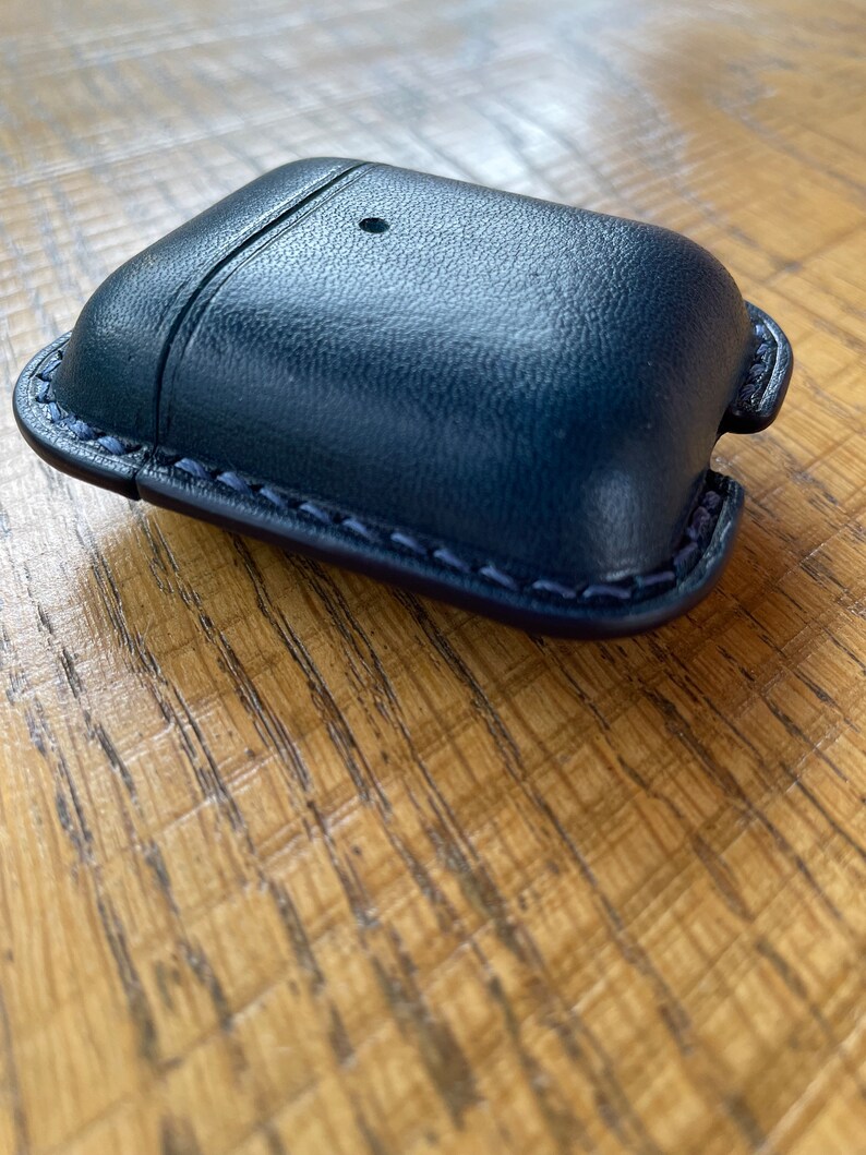 Puede incluir: Una funda de cuero azul oscuro con un borde cosido para AirPods.