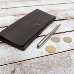 May include: A brown leather wallet with a silver pen and three gold coins on a white wooden surface.