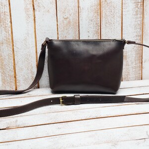 May include: A brown leather crossbody bag with a long adjustable strap and a gold buckle. The bag has a zipper closure and a flap.