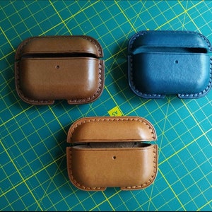 Puede incluir: Tres estuches de cuero para auriculares inal&aacute;mbricos. Un estuche es marr&oacute;n, otro es beige y el &uacute;ltimo es azul.