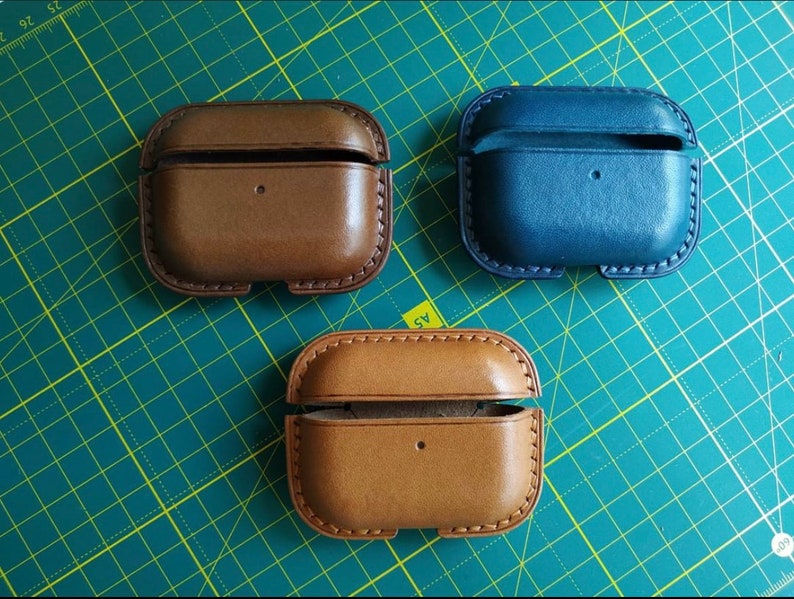 Puede incluir: Tres estuches de cuero para auriculares inal&aacute;mbricos. Un estuche es marr&oacute;n, otro es beige y el &uacute;ltimo es azul.