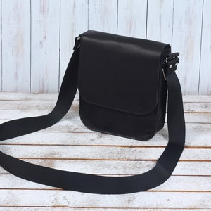 May include: A black leather shoulder bag with a long adjustable strap. The bag has a flap closure and a single compartment.