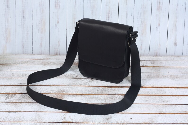 May include: A black leather shoulder bag with a long adjustable strap. The bag has a flap closure and a single compartment.