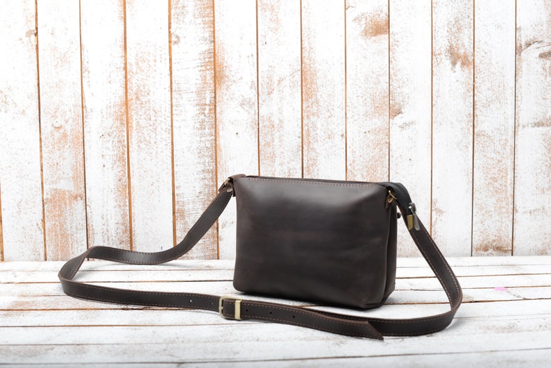 Peut inclure: Un sac &agrave; bandouli&egrave;re en cuir marron avec une longue sangle r&eacute;glable. Le sac a une fermeture &agrave; glissi&egrave;re et un rabat avec une boucle en m&eacute;tal.