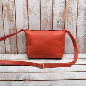 Peut inclure: Un sac &agrave; bandouli&egrave;re en cuir orange vif avec une longue sangle r&eacute;glable. Le sac a un design simple et minimaliste.