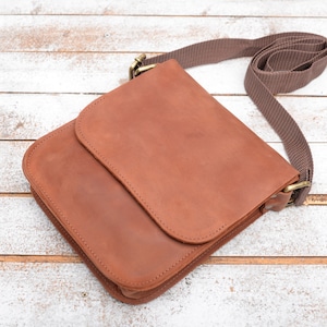 May include: A brown leather crossbody bag with a flap closure and a brown adjustable strap.