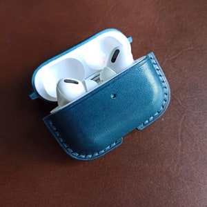 Puede incluir: Una funda de cuero azul oscuro para auriculares inal&aacute;mbricos. La funda tiene una cremallera y un peque&ntilde;o lazo en el lateral. Los auriculares son blancos y tienen un peque&ntilde;o micr&oacute;fono en el lateral.