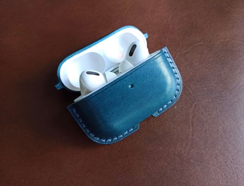 Puede incluir: Una funda de cuero azul oscuro para auriculares inal&aacute;mbricos. La funda tiene una cremallera y un peque&ntilde;o lazo en el lateral. Los auriculares son blancos y tienen un peque&ntilde;o micr&oacute;fono en el lateral.