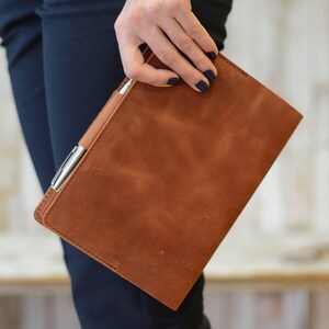 May include: A brown leather notebook with a pen tucked into the side pocket.