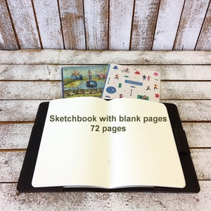 May include: Open sketchbook with a black cover and blank white pages. The text "Sketchbook with blank pages 72 pages" is printed on the front cover.