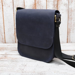 May include: A dark blue leather messenger bag with a black adjustable strap and brass hardware.