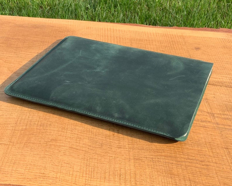 May include: A dark green leather laptop sleeve with a stitched edge.