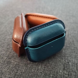Puede incluir: Dos estuches protectores para auriculares inal&aacute;mbricos. Un estuche es de cuero marr&oacute;n y el otro de cuero azul.