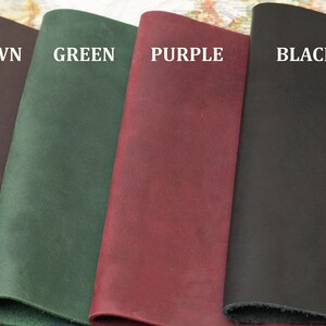 May include: Seven leather notebook covers in different colors: red, cognac, brown, green, purple, black, and blue. The covers are all made of the same type of leather and have a smooth, textured finish.