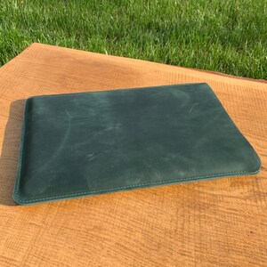 May include: A dark green leather laptop sleeve with a stitched edge.