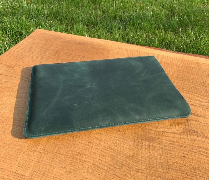May include: A dark green leather laptop sleeve with a stitched edge.