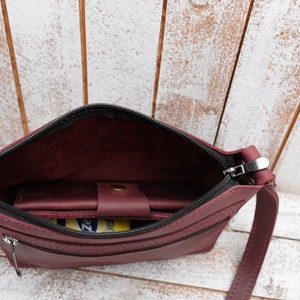 Peut inclure: Un sac &agrave; bandouli&egrave;re en cuir bordeaux avec une fermeture &agrave; glissi&egrave;re et un tirette de fermeture &eacute;clair noire. Le sac a une petite poche int&eacute;rieure et une longue bandouli&egrave;re.