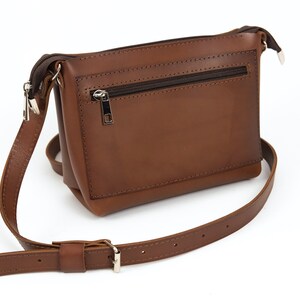 May include: A brown leather crossbody bag with a zippered pocket on the front. The bag has a long adjustable strap.