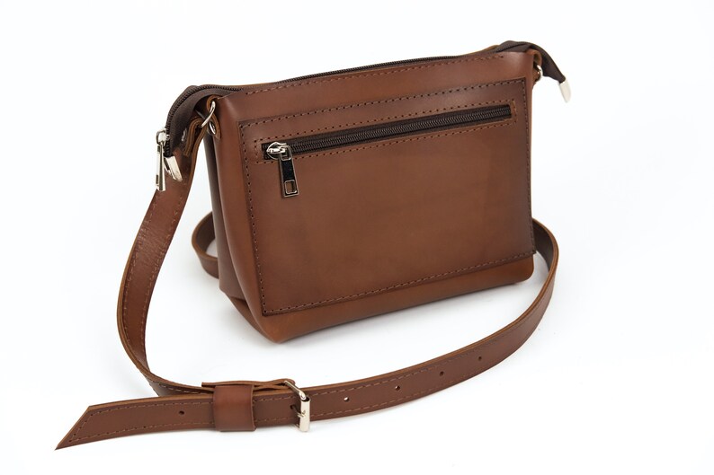 May include: A brown leather crossbody bag with a zippered pocket on the front. The bag has a long adjustable strap.