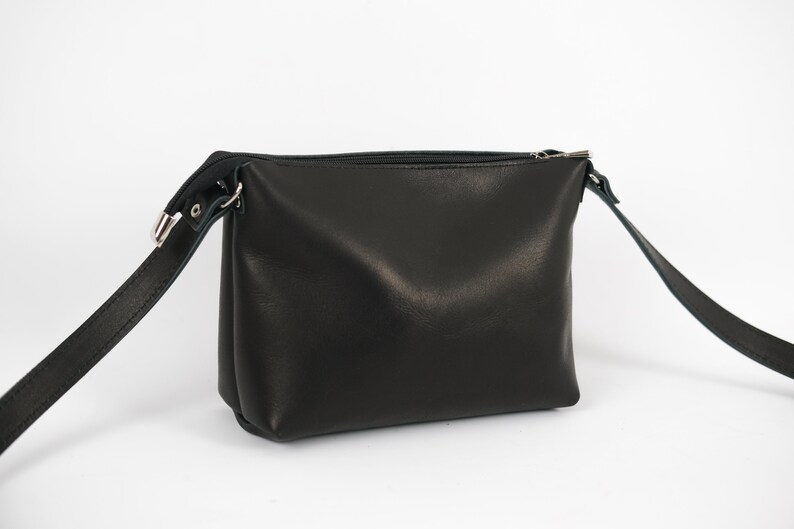 Pu&ograve; includere: Una borsa a tracolla in pelle nera con chiusura a zip e una lunga tracolla regolabile.