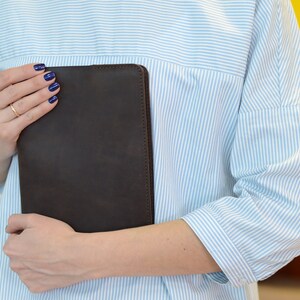 May include: A person holding a brown leather portfolio with a blue striped shirt.