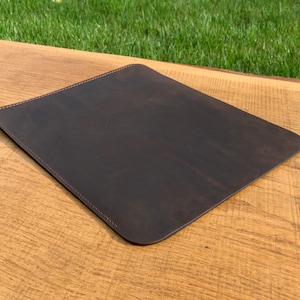 May include: A dark brown leather desk mat with stitched edges.