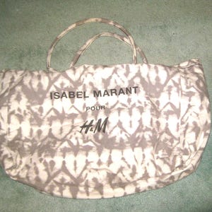 May include: A large, white and gray tote bag with a tie-dye pattern. The bag has black text that reads "Isabel Marant pour H&M".