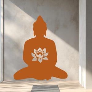 Puede incluir: Silueta naranja de un Buda sentado con una flor de loto en el pecho, sobre una pared texturizada. Una esterilla de yoga gris descansa sobre el suelo de madera, creando una est&eacute;tica serena y minimalista. La imagen evoca una sensaci&oacute;n de paz y atenci&oacute;n plena.