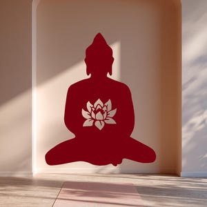 Puede incluir: Silueta roja de un Buda sentado con una flor de loto en el pecho, sobre una pared neutra. Una esterilla de yoga rosa descansa sobre el suelo de madera, creando una est&eacute;tica serena y minimalista.