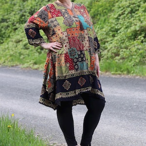 Könnte beinhalten: Eine bunte Patchwork-Tunika mit langen Ärmeln und V-Ausschnitt. Das Kleid weist eine Mischung aus Mustern und Farben auf, darunter Rot, Grün, Orange und Blau. Das Model trägt schwarze Leggings und Sandalen.