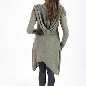 Può includere: Cardigan con cappuccio verde oliva a maniche lunghe e orlo asimmetrico. Il cardigan è realizzato in morbido tessuto a maglia e viene indossato con leggings grigio scuro. La modella è vista di spalle.