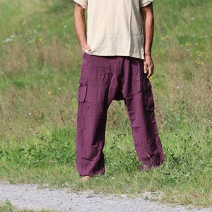 May include: A person wearing a light beige short-sleeved shirt and dark purple loose-fitting pants with pockets. The person is standing in a grassy field.