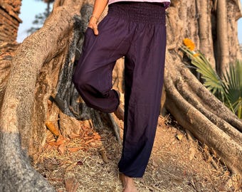 May include: A woman wearing a light purple halter top and dark purple harem pants. The top has a keyhole neckline and the pants have a gathered waistband. The outfit is worn outdoors near a large tree.