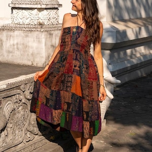 Könnte beinhalten: Eine Frau trägt ein braunes, mehrfarbiges Patchworkkleid mit Elefantenmuster. Das Kleid ist trägerlos und hat eine geraffte Taille. Sie steht vor einer weißen Wand mit kunstvollen Schnitzereien.