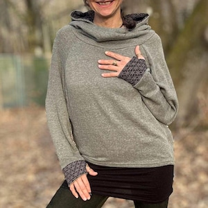 May include: A grey hooded sweatshirt with patterned cuffs and collar. The long-sleeved top has a cowl neck and a relaxed fit. The cuffs and collar feature a geometric design. The bottom of the image shows the text "LACOSY" and the website address.