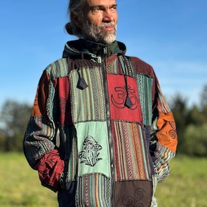 Może przedstawiać: Kurtka z kapturem w stylu patchwork z różnymi wzorami i kolorami, w tym czerwonym, zielonym i brązowym. Kurtka ma zapięcie na zamek błyskawiczny, grafikę grzyba i symbol Om. Odzież składa się z różnych łat materiału.