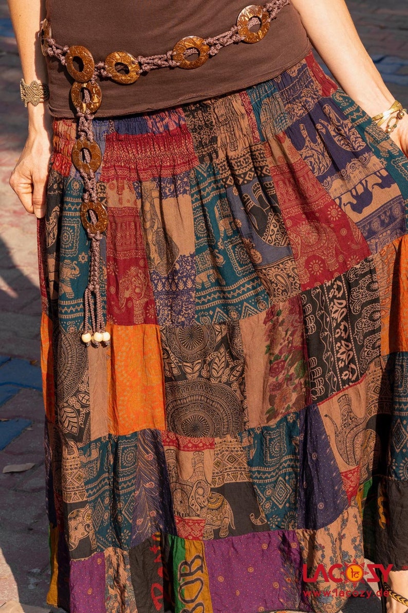 Puede incluir: Una falda larga de retazos multicolores con un cintur&oacute;n marr&oacute;n adornado con grandes cuentas redondas de madera. La falda tiene una variedad de patrones, incluyendo elefantes, paisley y dise&ntilde;os geom&eacute;tricos.
