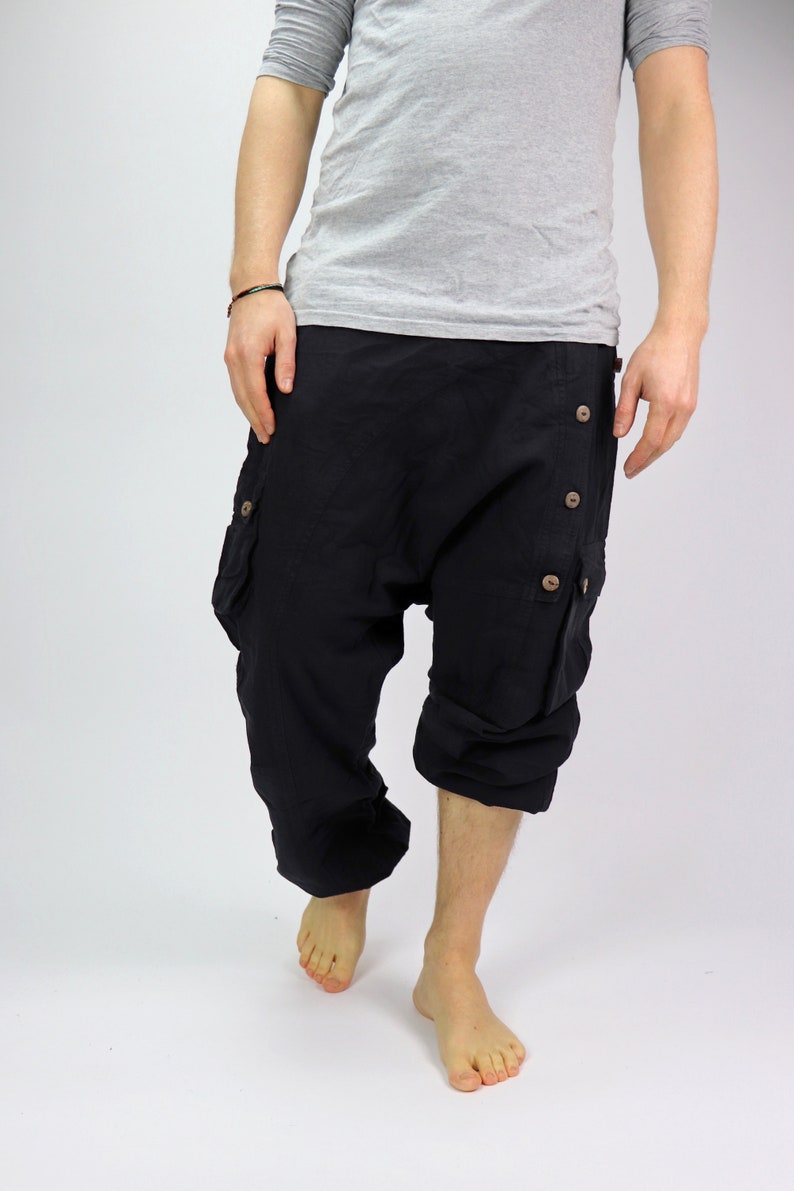 May include: Black cotton pants with a loose, baggy fit and multiple buttons down the side. The pants have a cargo pocket on each leg.
