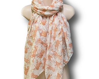 May include: A cream-coloured scarf featuring a repeating pattern of orange leopard print. The scarf is draped over a mannequin. The scarf is made of a lightweight material, suitable for warmer weather.